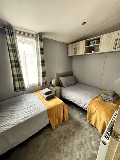 Twin bedroom at Tŷ'r Môr with two single beds, mustard throws and fresh towels
