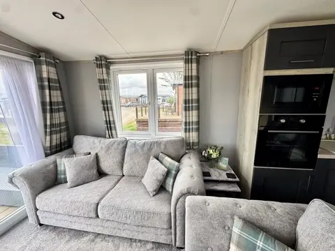 Comfortable sofa seating in the living area of Tŷ'r Môr, with tartan curtains and natural light